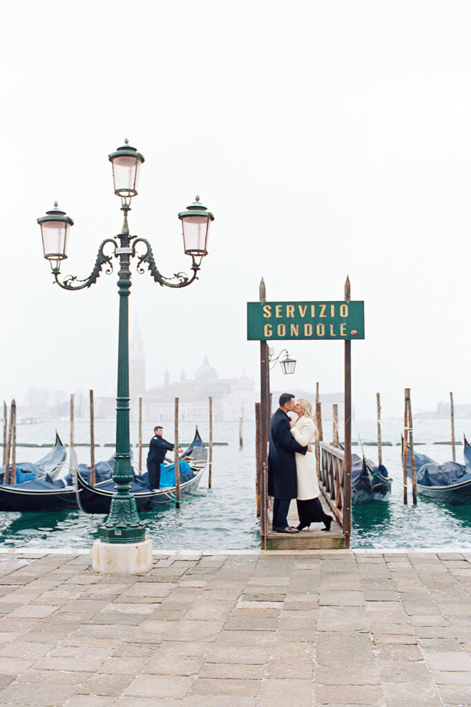 A romantic couple sharing a moment at the gondola dock near St. Mark’s Square in Venice—hire a Venice photographer to capture your love against this iconic backdrop.